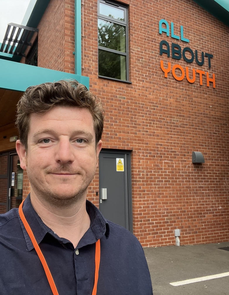 Neil outside All About Youth, with the charity name visible on the building